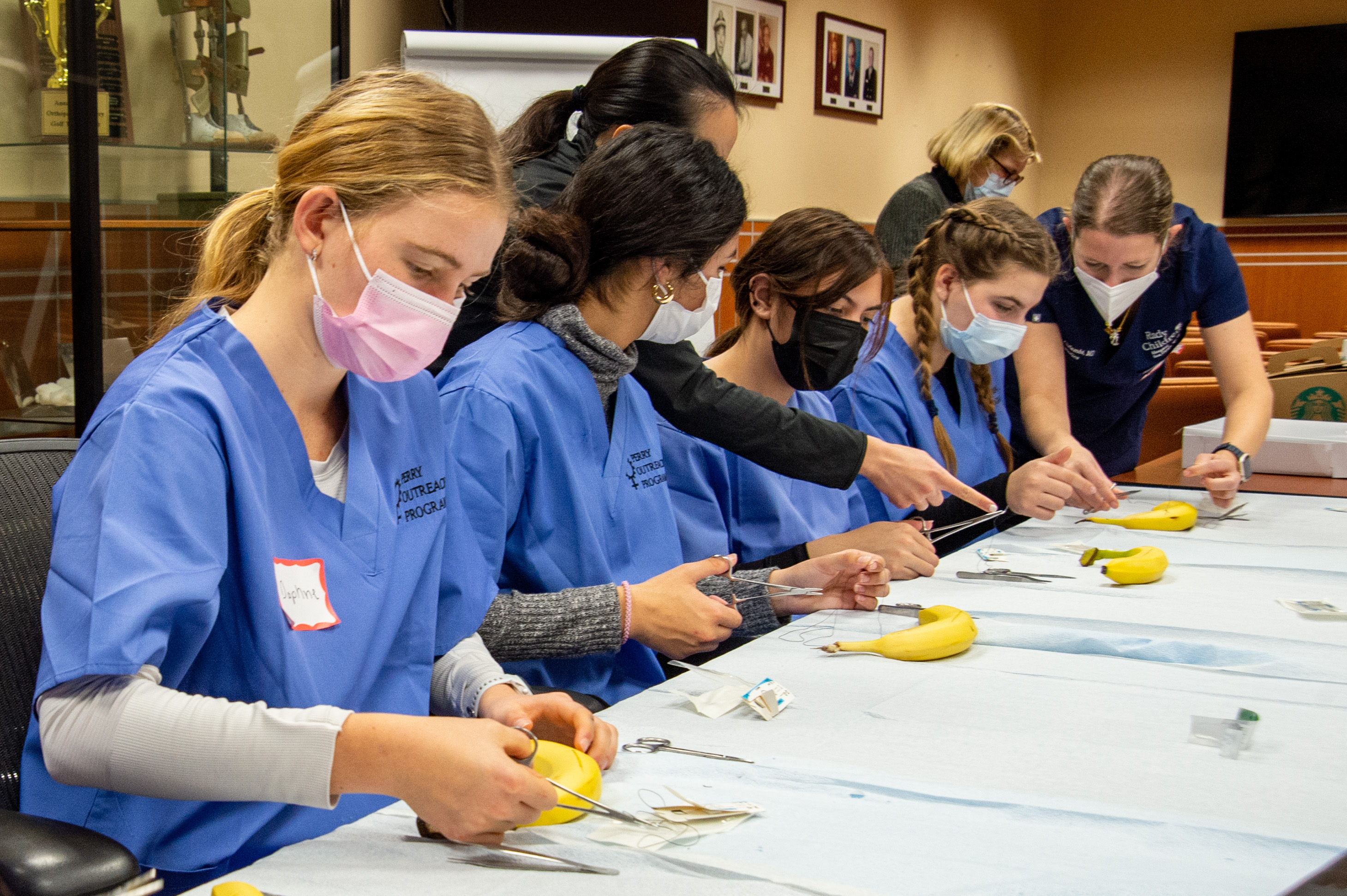 Medical students at a table, practicing surgery on bananas